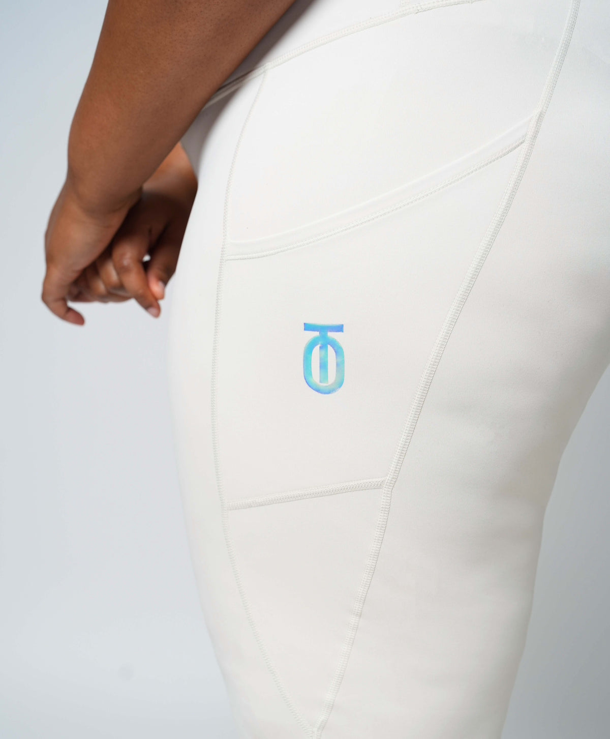 Close-up of cream Take One Fade Leggings showing the light blue Take One logo on the upper thigh.