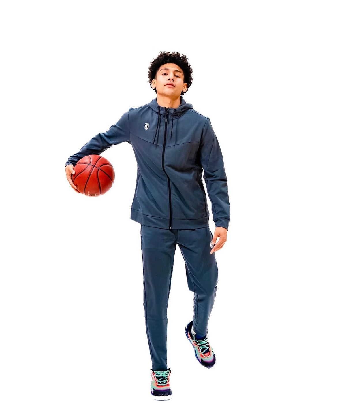 Athlete wearing the navy blue Take One Sportswear ROAM Sweatsuit while holding a basketball against a white studio background.
