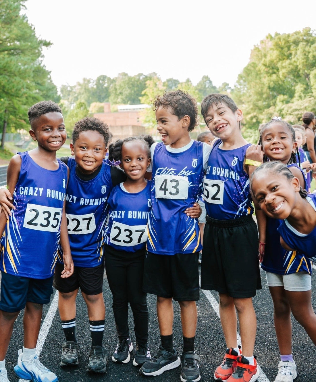 Seven young Raleigh Crazy Running athletes smiling together in blue team uniforms as part of their partnership with Take One Sportswear.