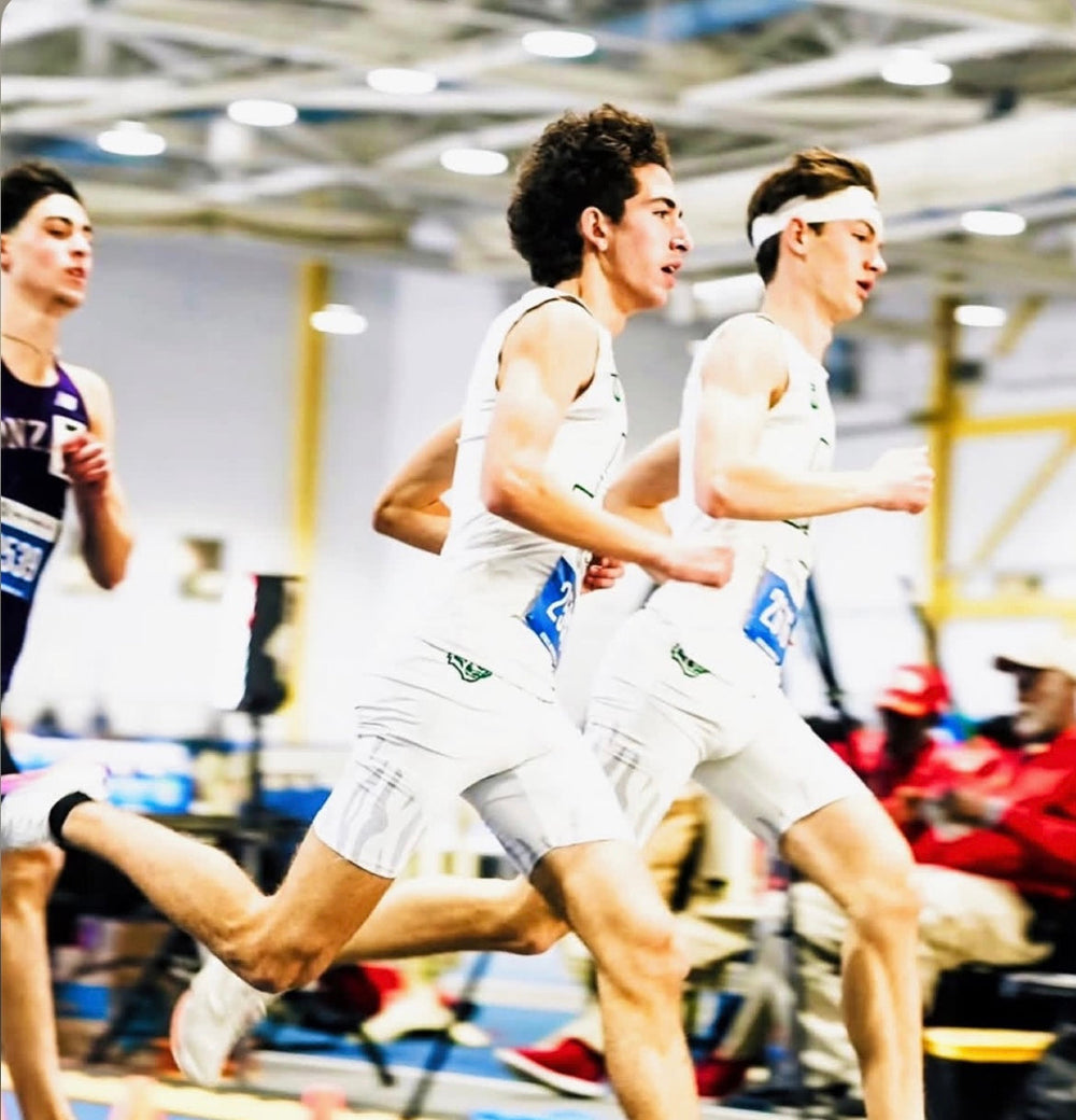 Indoor track athletes racing in custom Take One Sportswear uniforms.