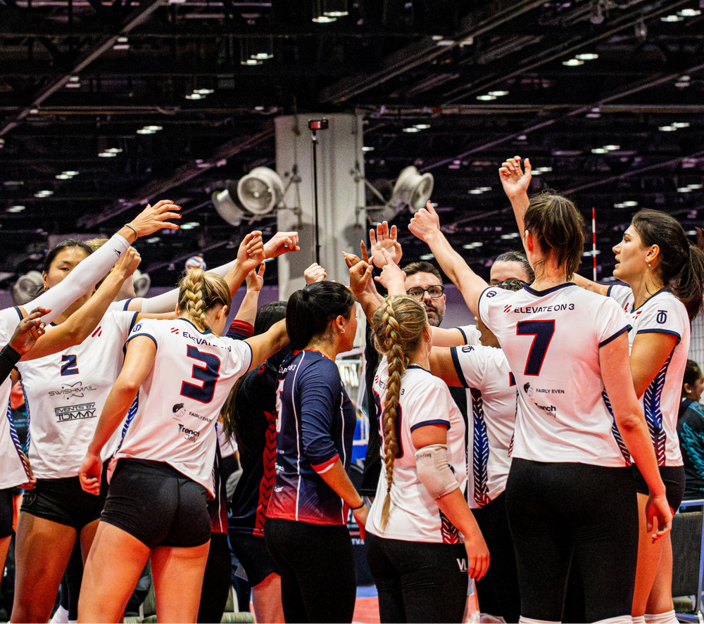 Elevate On 3 volleyball team huddling in custom Take One Sportswear uniforms during competition.