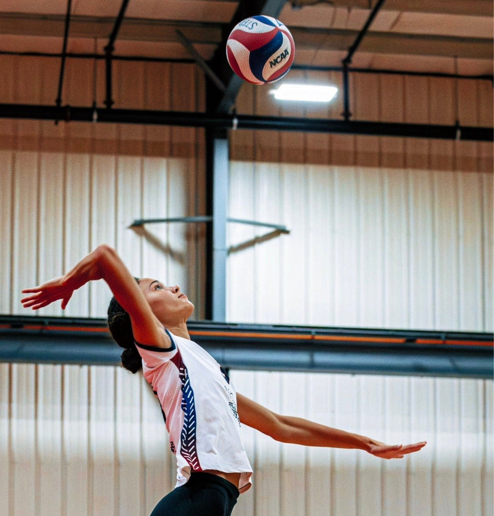 Volleyball player serving in a custom Take One Sportswear uniform during an indoor match.