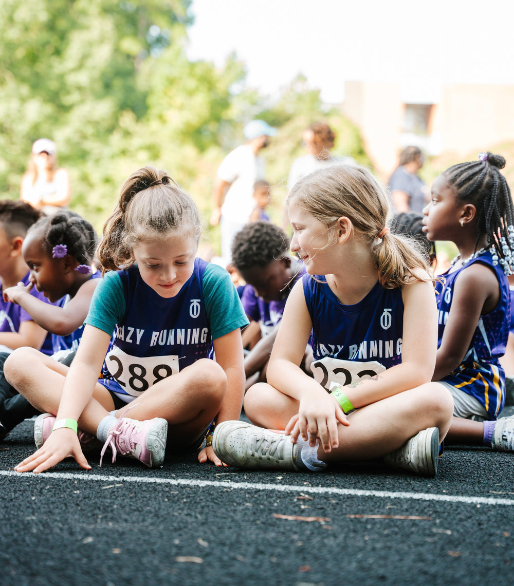 Youth track athletes wearing custom Take One Sportswear uniforms while sitting together at a track meet.
