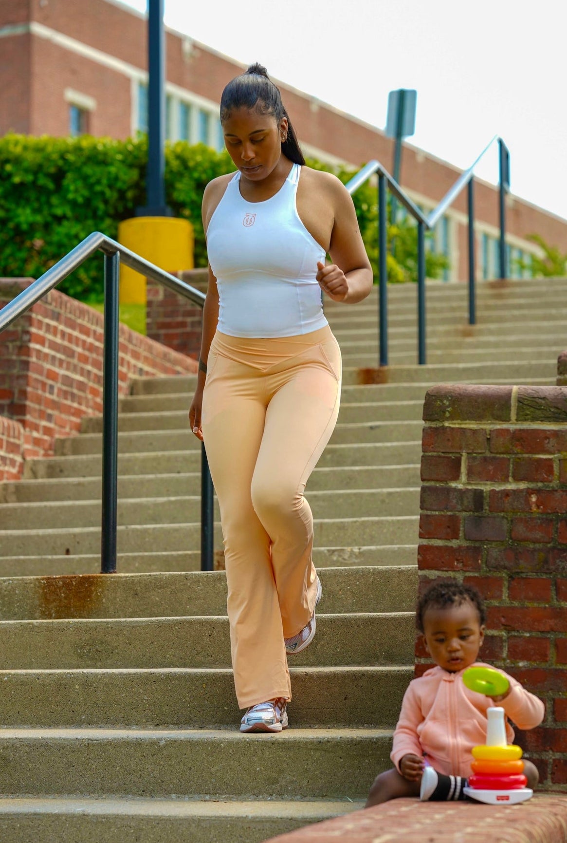 Woman modeling peach Take One Sportswear Bliss Leggings and a white tank top in an outdoor lifestyle photoshoot.