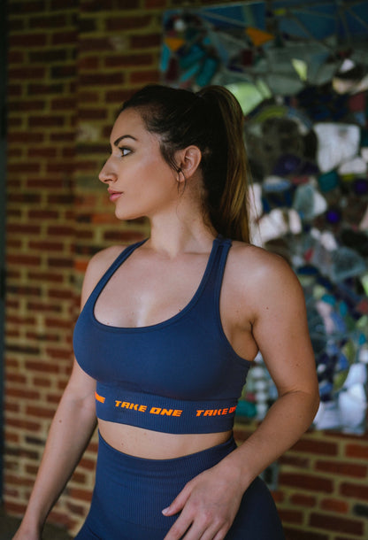 Woman modeling the navy Drift Sports Bra with orange trim by Take One Sportswear during an outdoor activewear photoshoot.