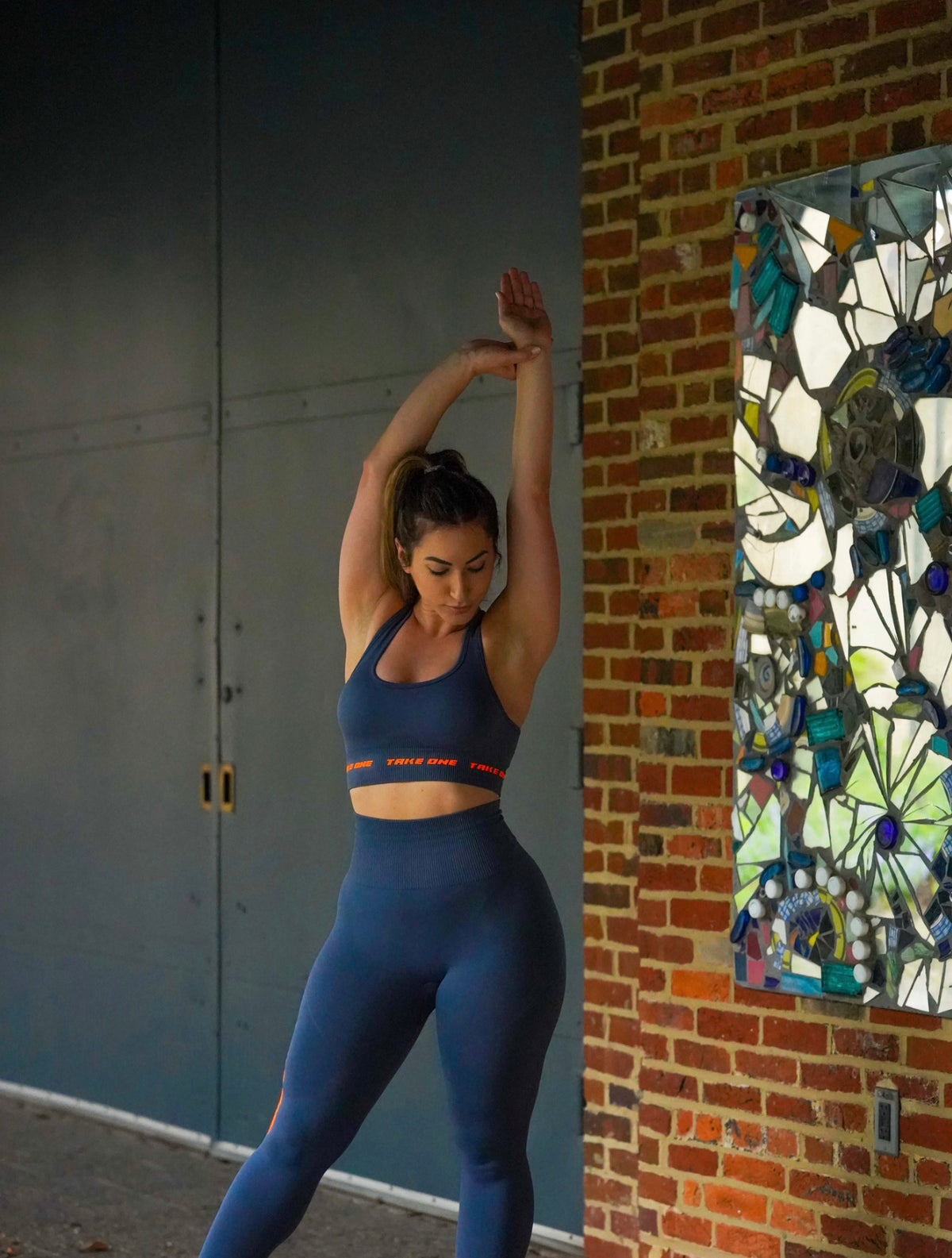Woman wearing a navy Take One Sportswear Drift Sports Bra and coordinating leggings while stretching outdoors.