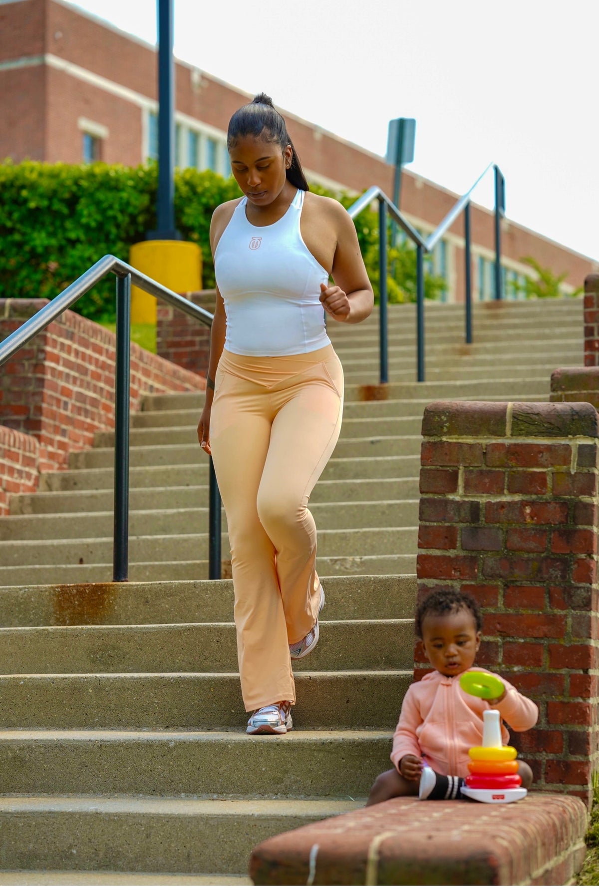 Woman wearing a white Take One Sportswear Impose Compression Tank and peach leggings near outdoor steps.
