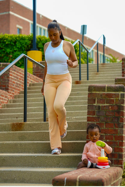 Woman wearing a white Take One Sportswear Impose Compression Tank and peach leggings near outdoor steps.