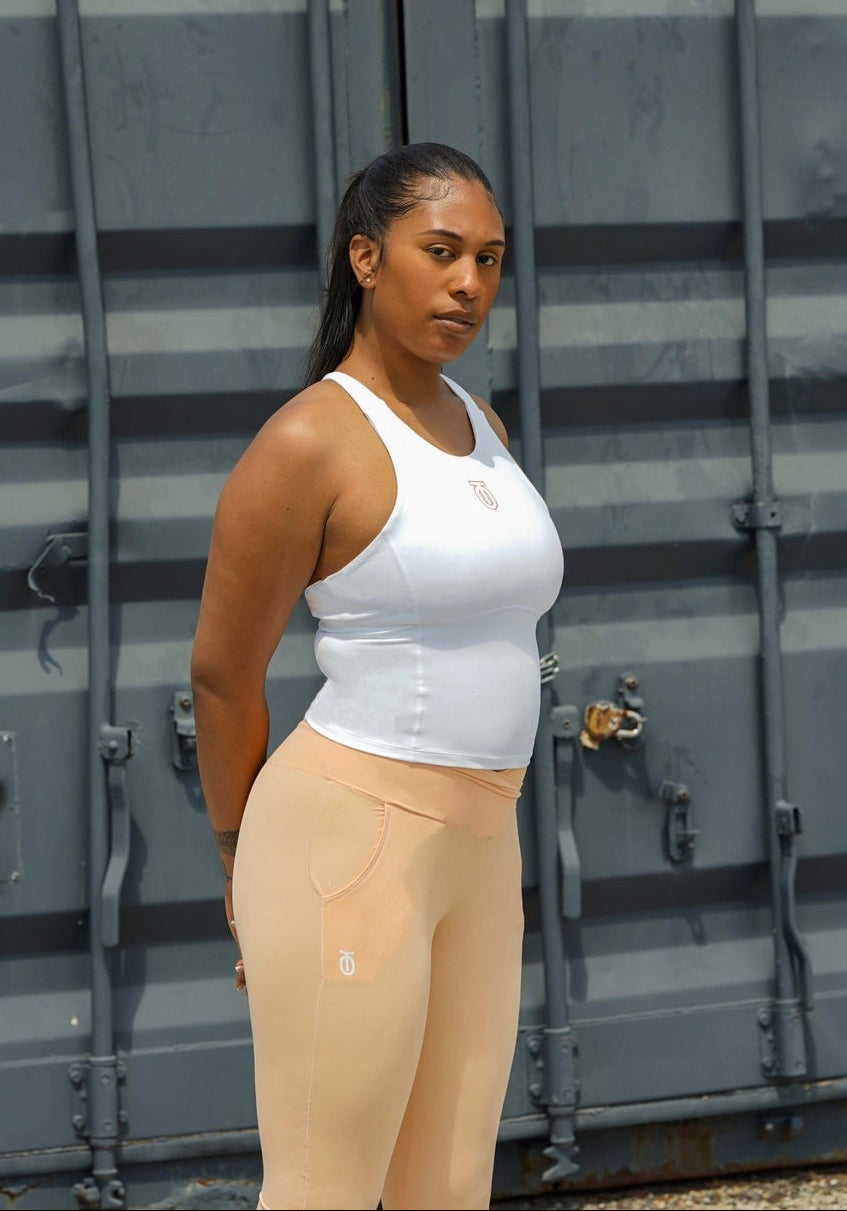 Woman modeling the white Take One Impose Compression Tank with peach-colored leggings in an outdoor urban setting.