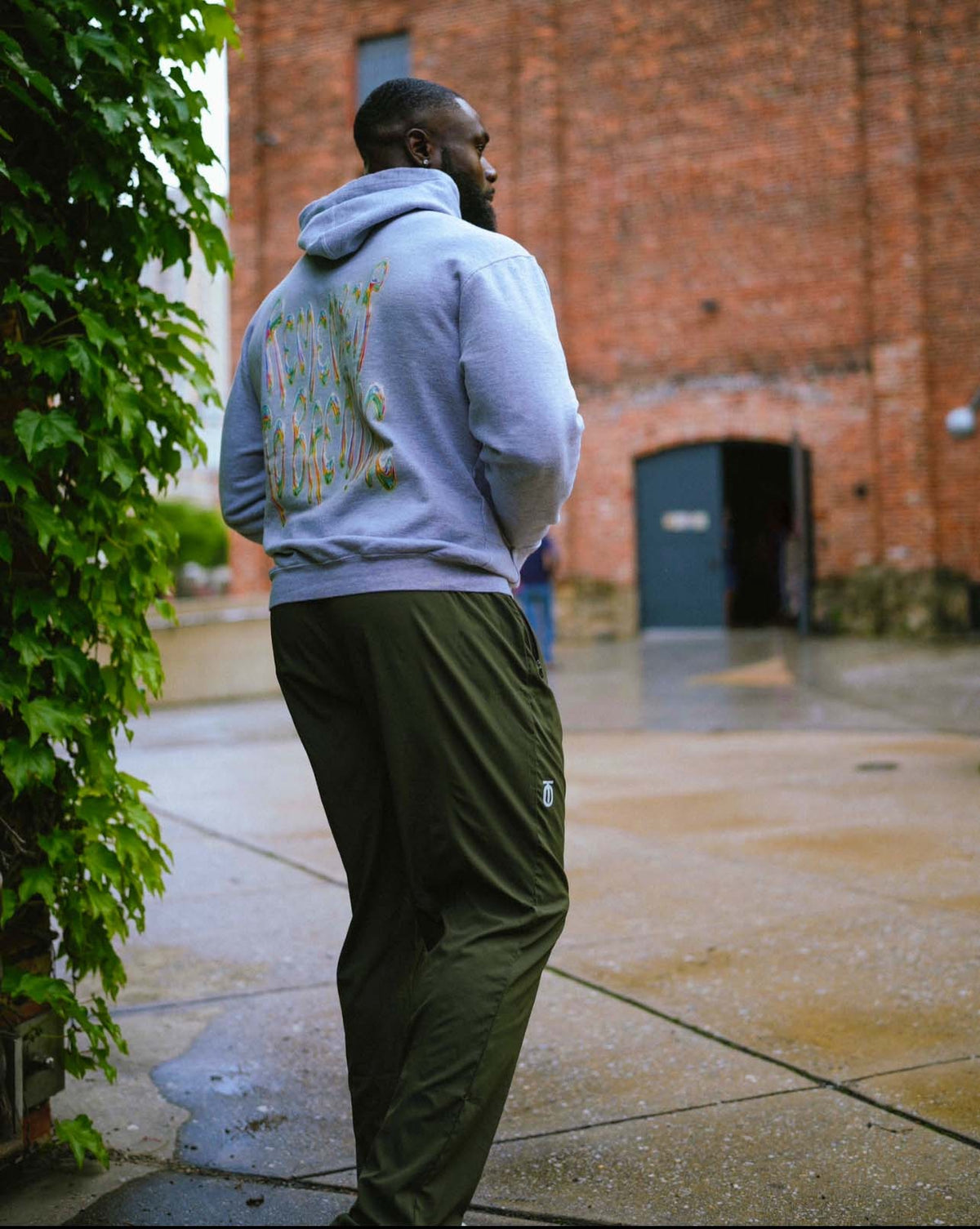Rear view of men's olive Integrated Flow Performance Joggers by Take One Sportswear styled with a grey hoodie.