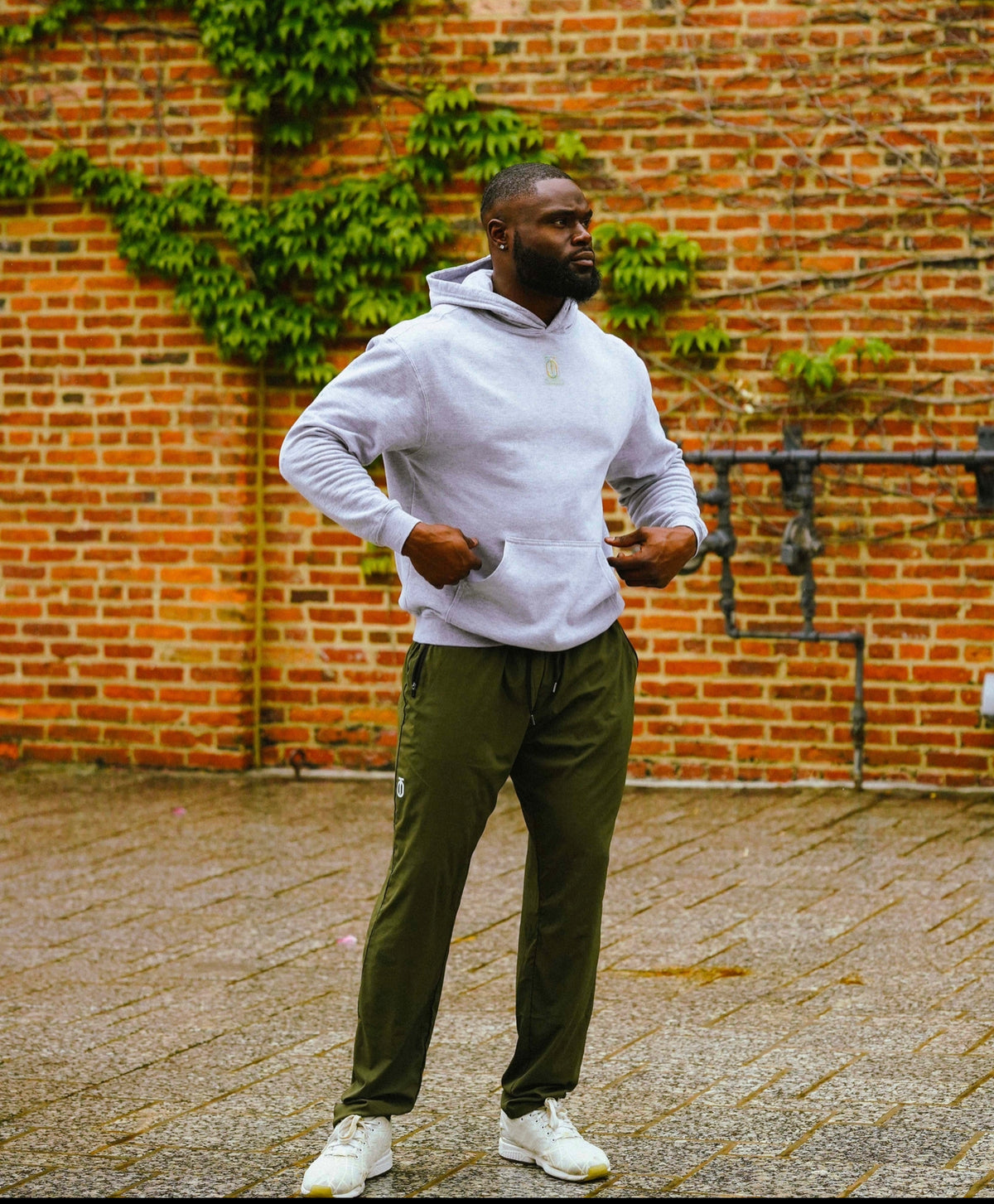 Man wearing olive green Integrated Flow Performance Joggers by Take One Sportswear with a grey hoodie in an outdoor urban setting.