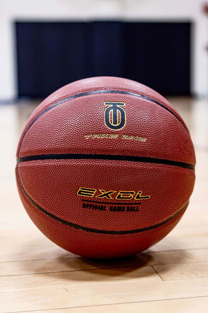 Front view of the reddish-brown Take One EXCL Basketball with EXCL graphics and Take One Sportswear logo on a wood floor.