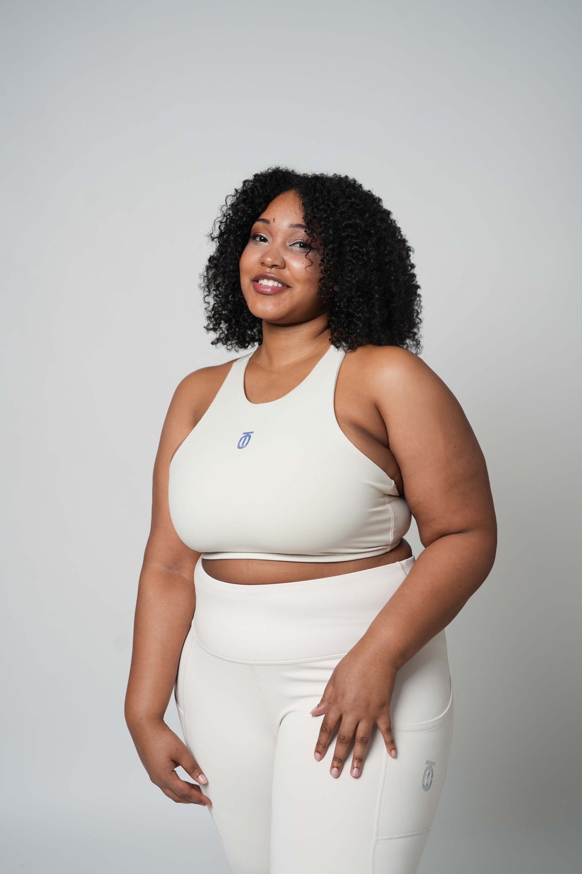 Woman modeling cream Take One Fade high-waisted leggings with matching sports bra in a studio setting.