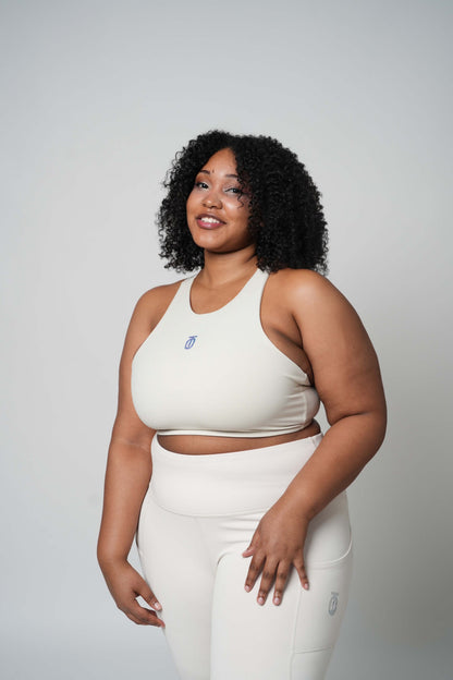 Woman modeling cream Take One Fade high-waisted leggings with matching sports bra in a studio setting.