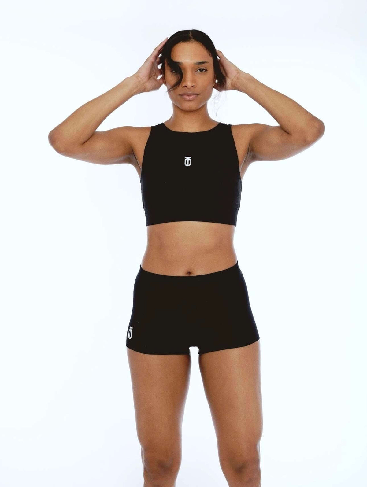 Woman posing with raised hands in a black Take One Sportswear Form High Neck Tank and black shorts.