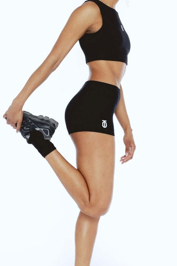 Woman stretching her leg in black FormPro athletic shorts by Take One Sportswear against a white studio background.