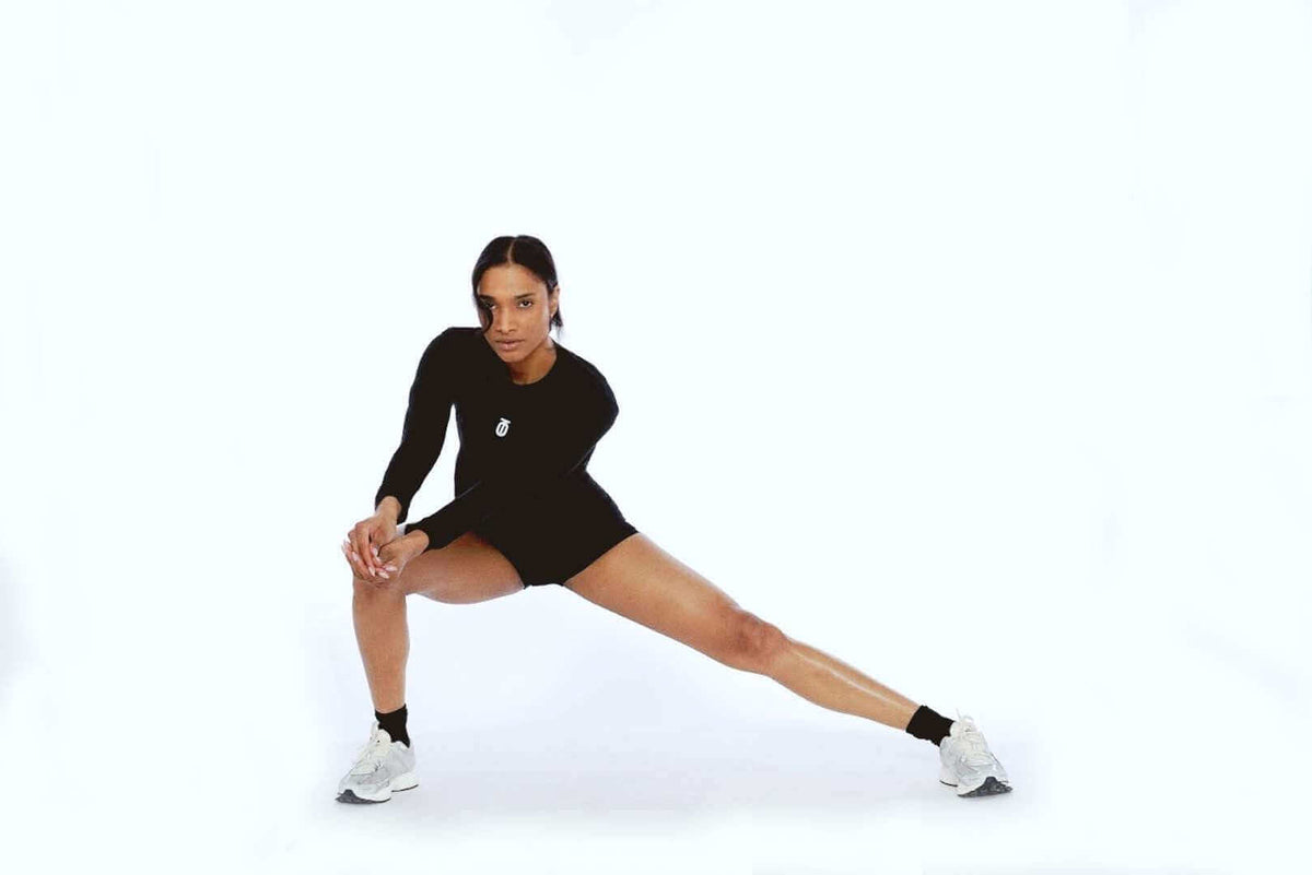 Woman performing a lateral lunge in black Take One Sportswear FormPro Shorts and a black long-sleeve top.