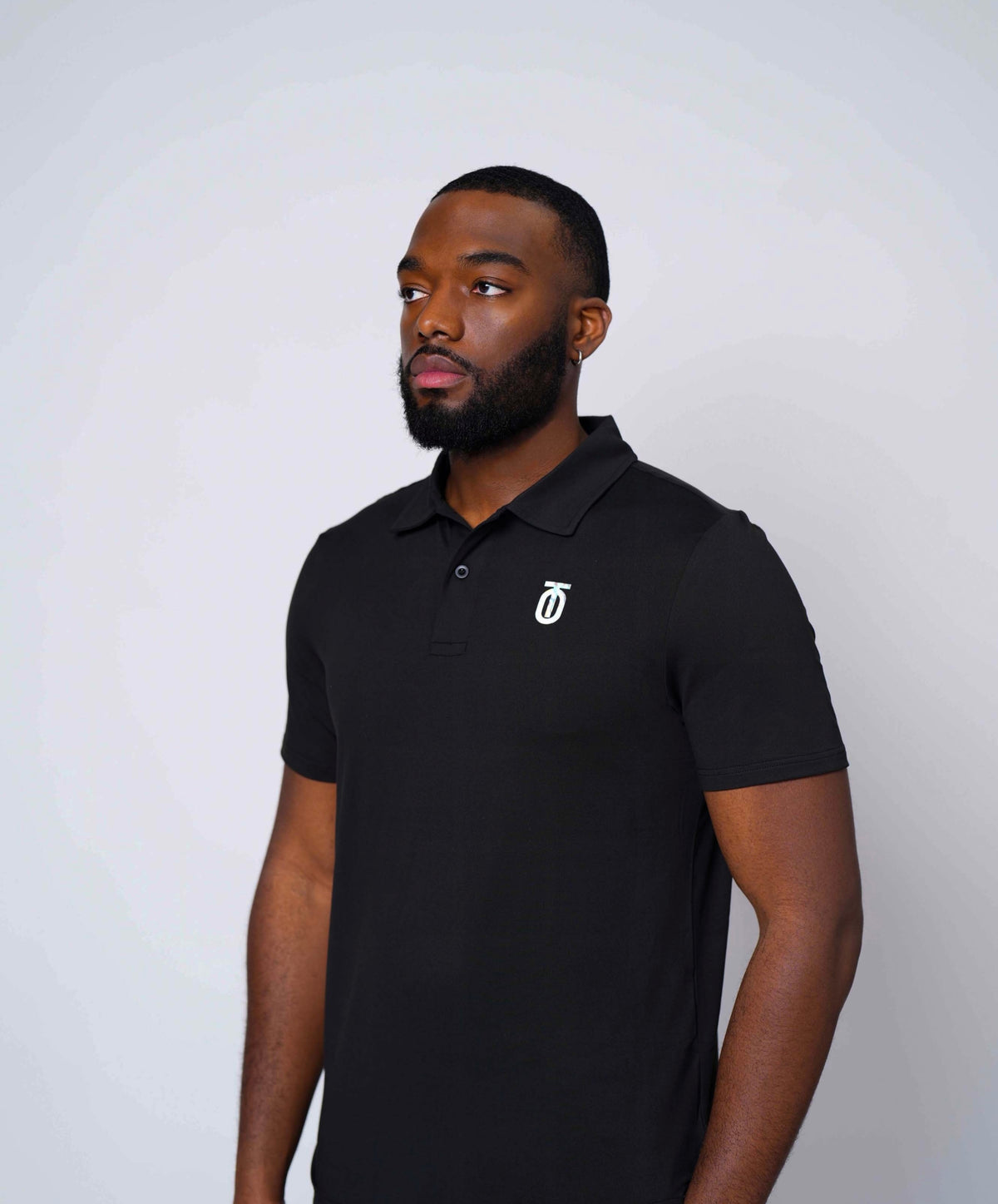 Male model wearing a black Take One Journey Performance Polo with white chest logo against a light studio background.