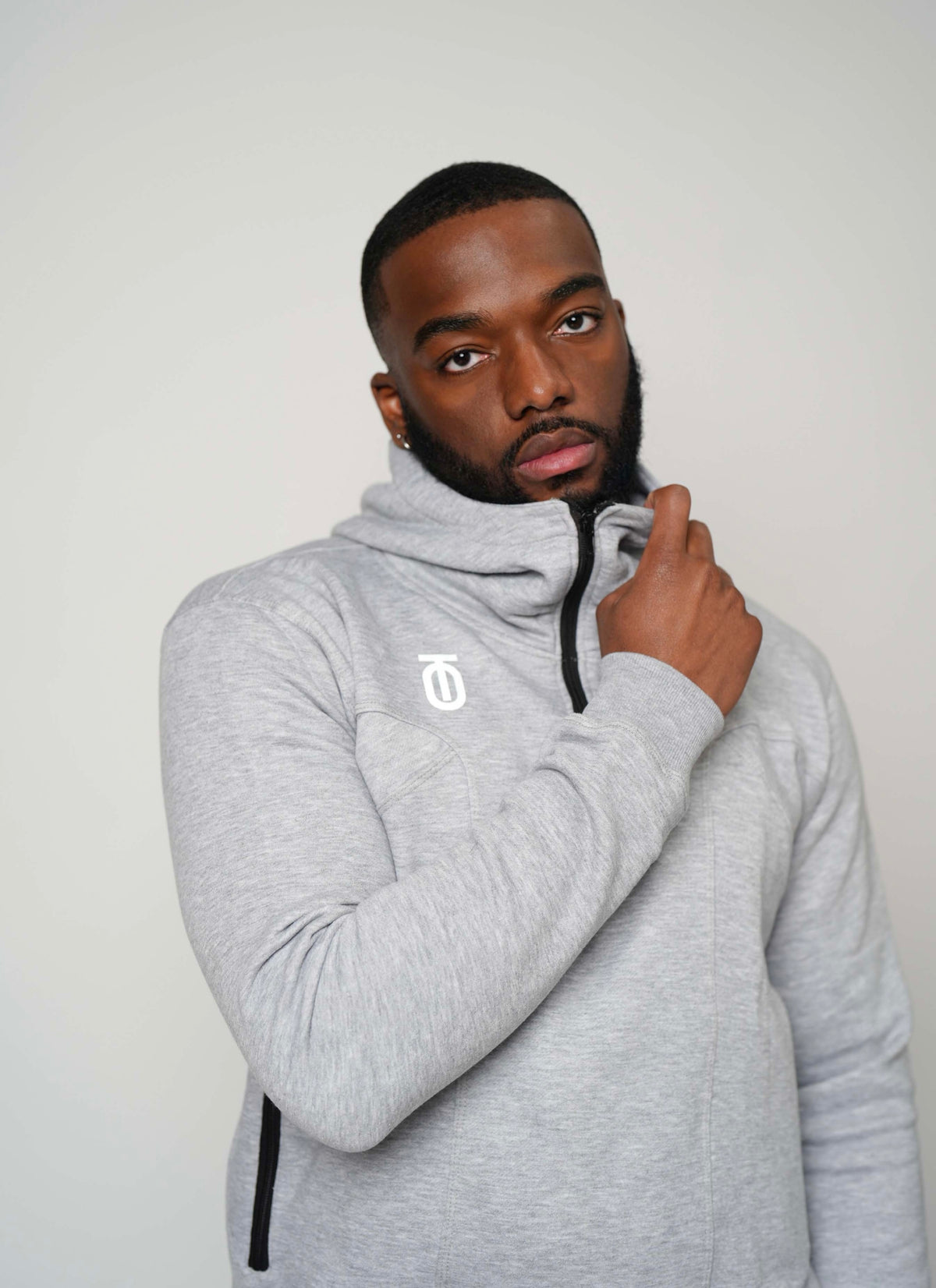 Male model adjusting the collar of a light grey Take One PeakPro Fleece Pullover with a black zipper and white Take One chest logo.