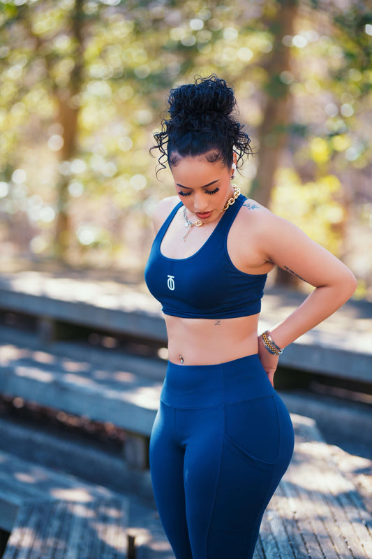 Woman wearing a navy blue Take One Sportswear Power Mesh sports bra and matching leggings, standing outdoors and looking down.