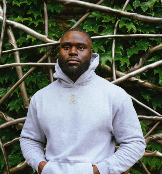 Model standing outdoors in front of greenery wearing a light gray Take One Sportswear Remember to Breathe pullover hoodie.