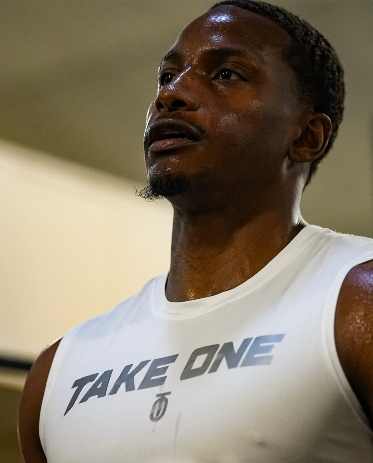 Close-up of a muscular athlete wearing the white Take One Dimension 2.0 Compression Tank, showing the Take One Sportswear chest lettering and sleeveless athletic fit.