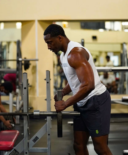 Male athlete wearing the white Take One Sportswear Dimension 2.0 sleeveless compression training top during a strength-training session in a gym.