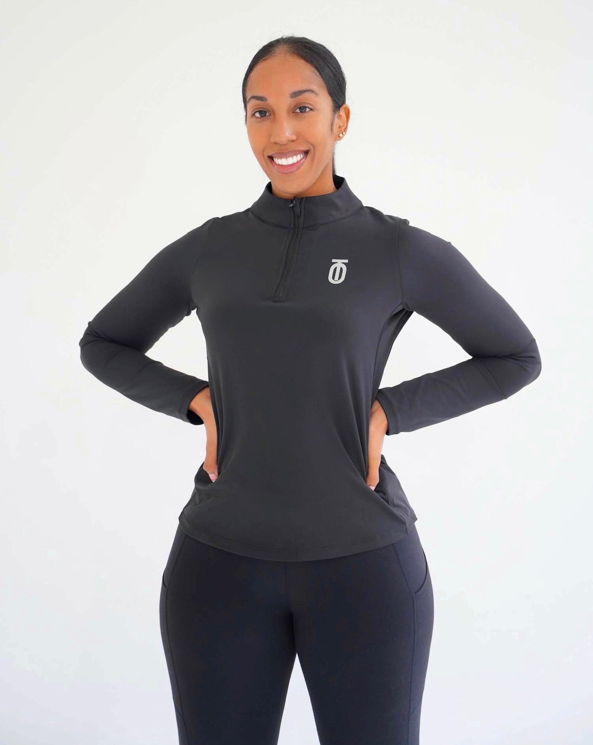 Woman modeling the black Take One Therma-FIT long-sleeve training top with raised collar and white Take One chest logo against a white studio background.