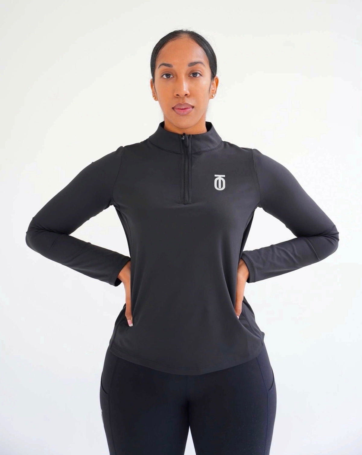 Full front view of a woman wearing the black Take One Therma-FIT fitted long-sleeve performance top and matching black leggings with hands on hips.