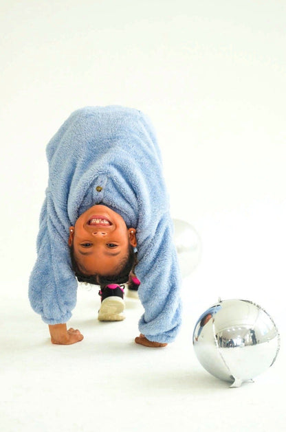 Child wearing a light blue Take One Sportswear Tundra fleece hoodie while bending forward to play near a soccer ball in a studio.